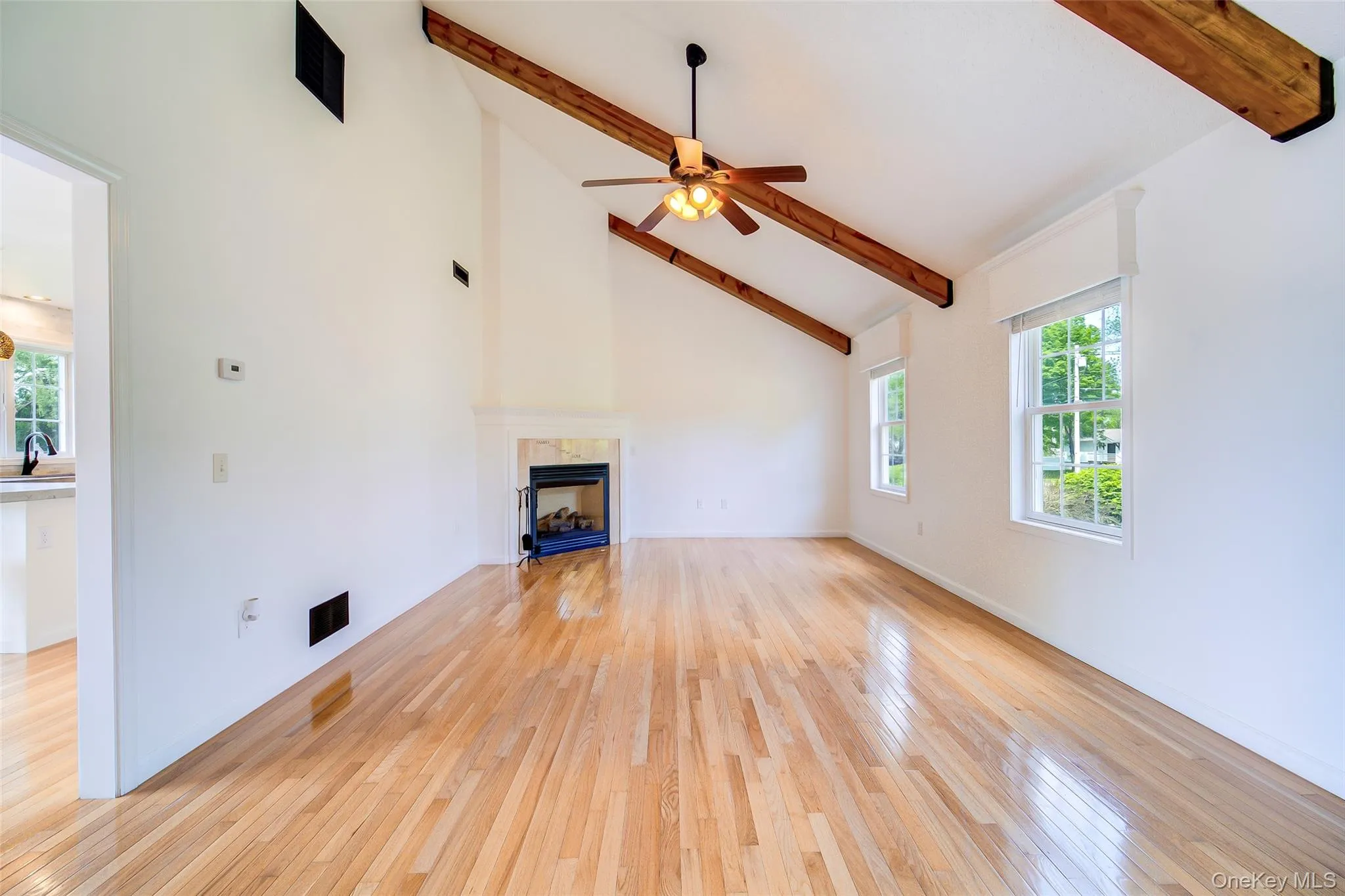Vaulted ceiling with exposed wood beams, a central ceiling fan, and light wood-finish flooring Vaulted ceiling with exposed wood beams, a central ceiling fan, and light wood-finish flooring