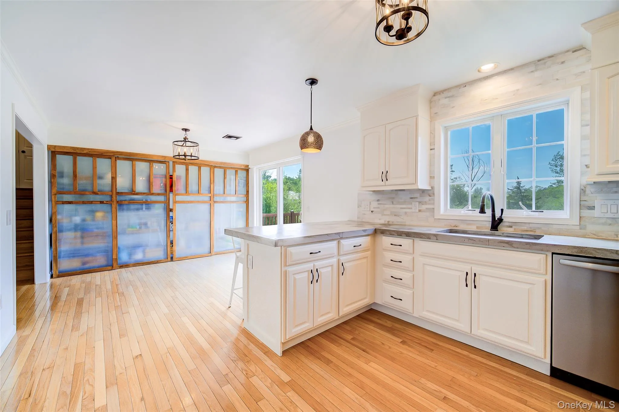 Kitchen featuring light-finish wood flooring, white cabinetry with dark hardware, and a center island with countertop seating Kitchen featuring light-finish wood flooring, white cabinetry with dark hardware, and a center island with countertop seating