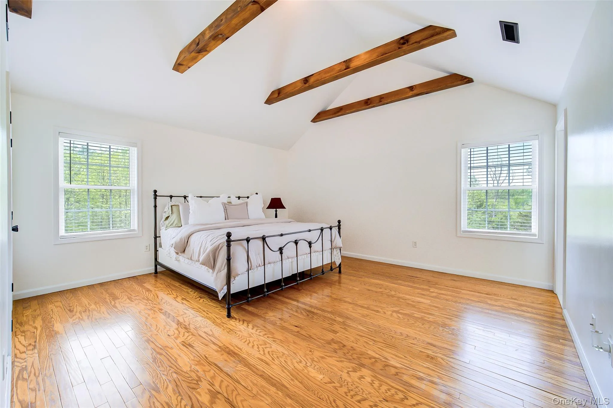 Vaulted ceiling with exposed wood beams, wood-finish flooring, and white walls Vaulted ceiling with exposed wood beams, wood-finish flooring, and white walls