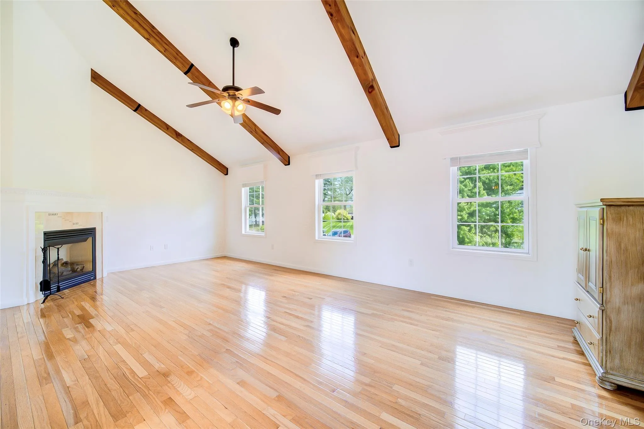 Spacious living room featuring vaulted ceilings with exposed wood beams, a ceiling fan, and light wood-finish flooring Spacious living room featuring vaulted ceilings with exposed wood beams, a ceiling fan, and light wood-finish flooring