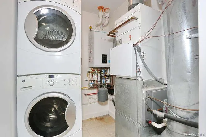 Laundry room with stacked washing machine and dryer, tankless water heater, and light tile patterned floors Laundry room with stacked washing machine and dryer, tankless water heater, and light tile patterned floors