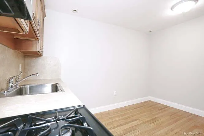 Kitchen featuring a sink, light countertops, range hood, light wood finished floors, and decorative backsplash Kitchen featuring a sink, light countertops, range hood, light wood finished floors, and decorative backsplash