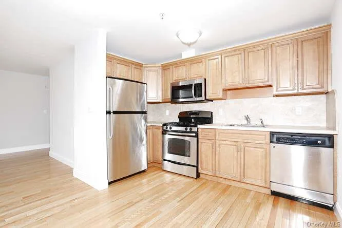 Kitchen featuring stainless steel appliances, light wood-type flooring, light countertops, and backsplash Kitchen featuring stainless steel appliances, light wood-type flooring, light countertops, and backsplash