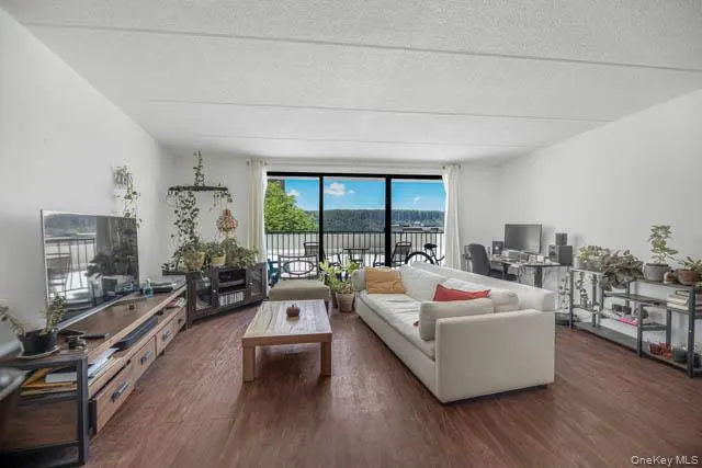 Spacious living area featuring expansive wood-finish flooring, white walls, and a large balcony with outdoor railing Spacious living area featuring expansive wood-finish flooring, white walls, and a large balcony with outdoor railing