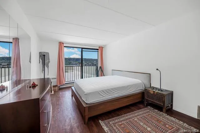 Bedroom featuring a full-wall mirror, sliding glass doors, dark wood-finish flooring, and a private balcony with metal railings and expansive outdoor scenery Bedroom featuring a full-wall mirror, sliding glass doors, dark wood-finish flooring, and a private balcony with metal railings and expansive outdoor scenery