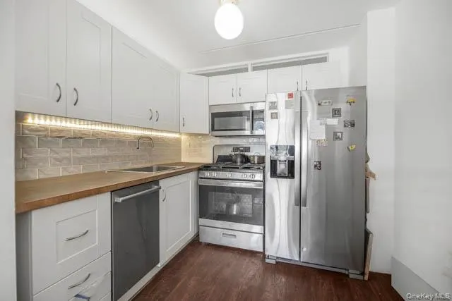 Kitchen featuring white shaker-style cabinetry, wood-finish countertops, and a subway tile backsplash with under-cabinet lighting Kitchen featuring white shaker-style cabinetry, wood-finish countertops, and a subway tile backsplash with under-cabinet lighting