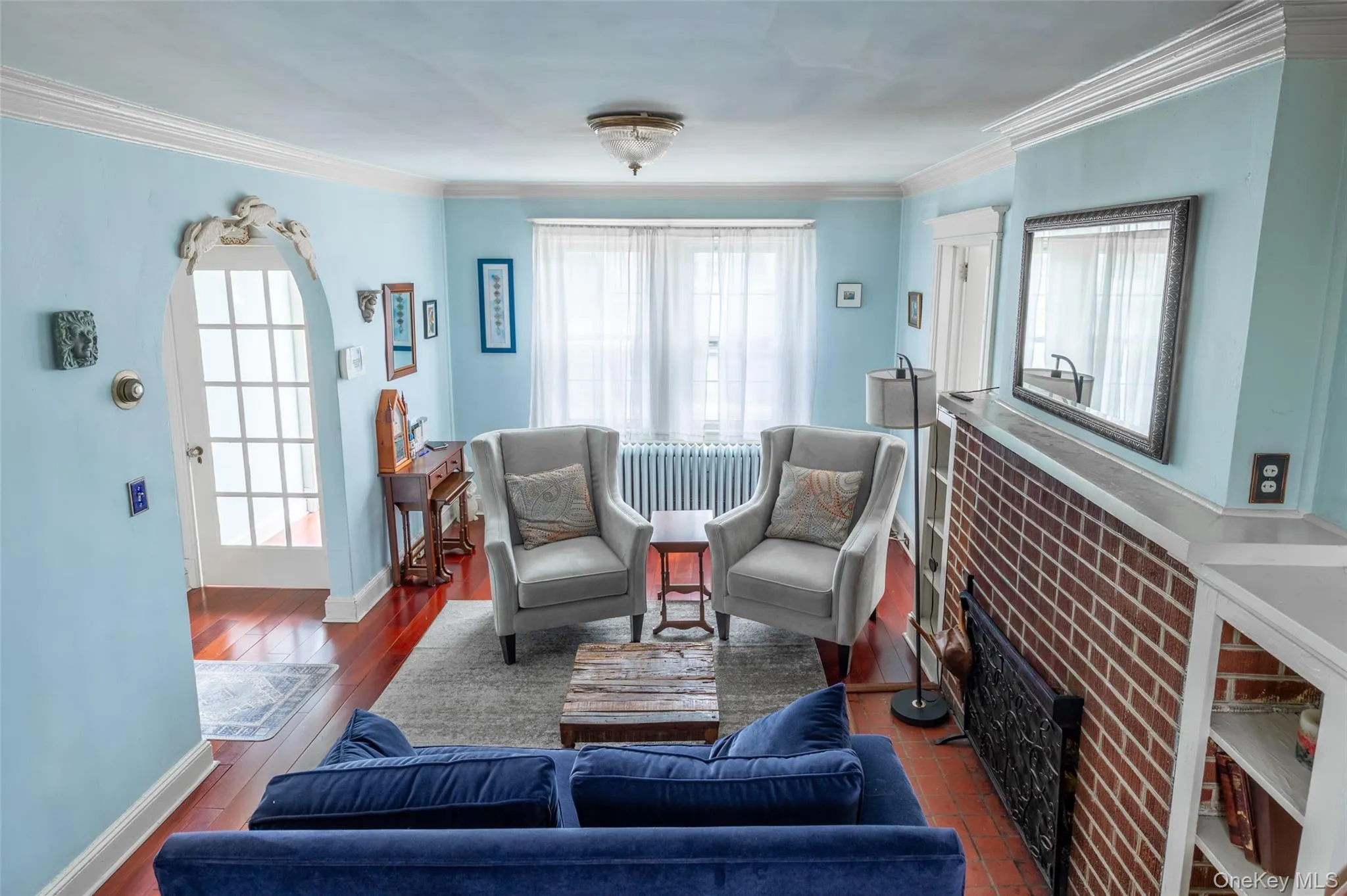 Living area featuring wood-finish flooring, an arched doorway with decorative molding, and crown molding Living area featuring wood-finish flooring, an arched doorway with decorative molding, and crown molding