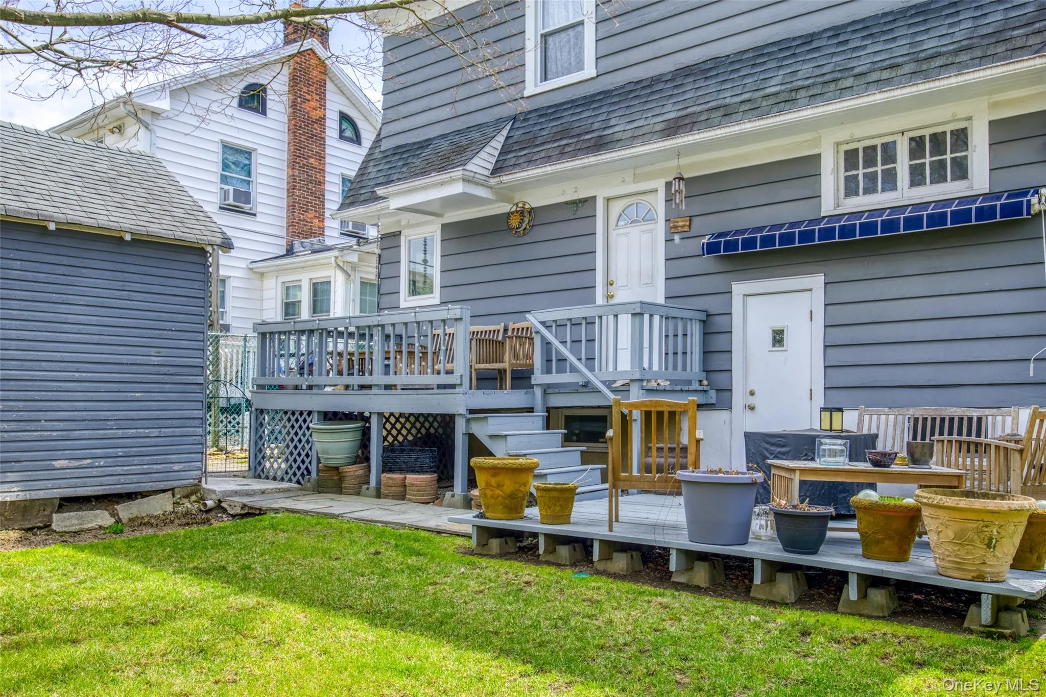 Expansive backyard featuring a manicured lawn, a detached storage shed, a multi-level wooden deck, and a blue retractable awning Expansive backyard featuring a manicured lawn, a detached storage shed, a multi-level wooden deck, and a blue retractable awning