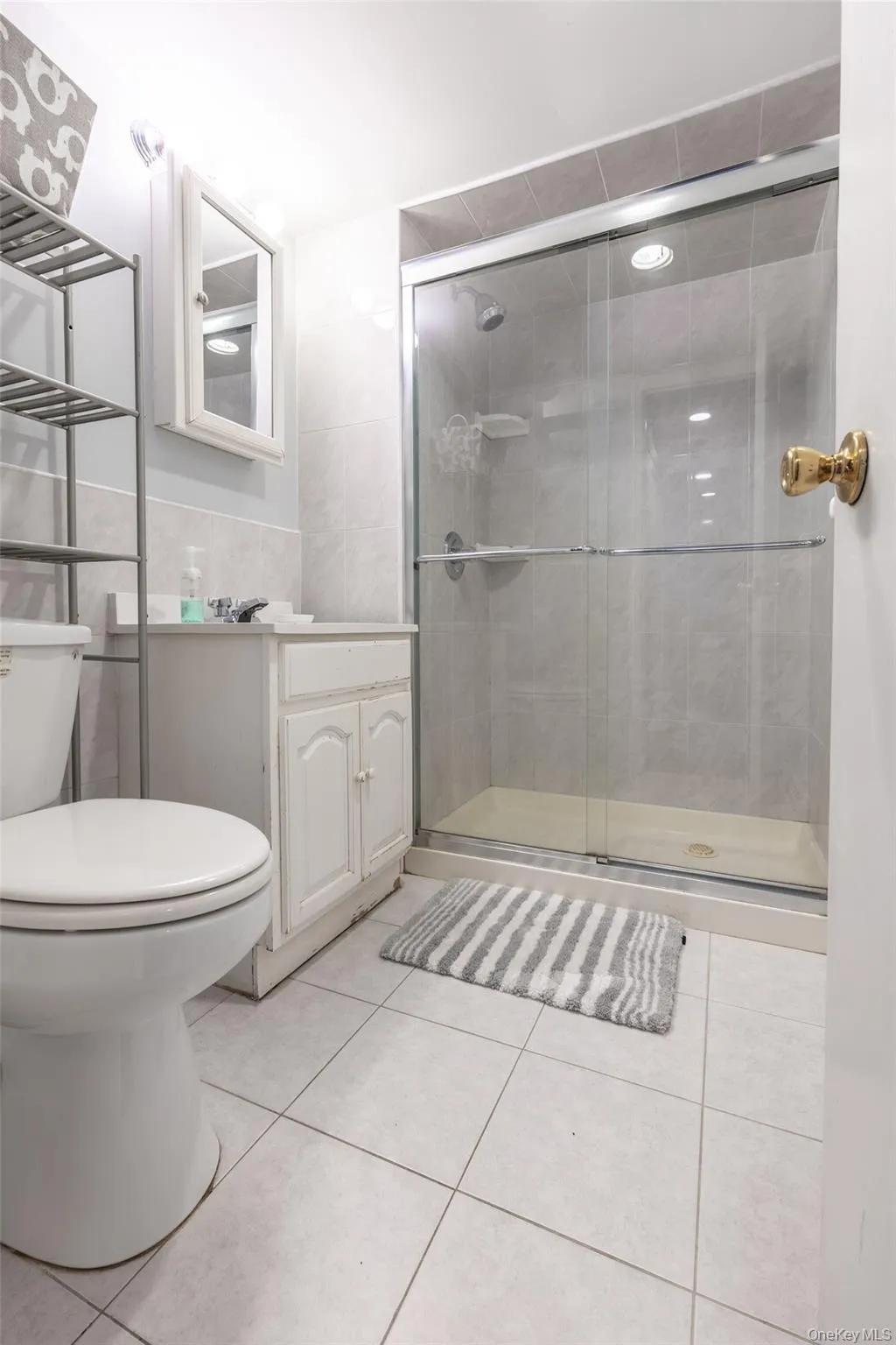 Three-quarter bathroom featuring a glass-enclosed shower, white vanity with cabinet storage, wall-mounted medicine cabinet with mirror, ceramic tile flooring, and a toilet Three-quarter bathroom featuring a glass-enclosed shower, white vanity with cabinet storage, wall-mounted medicine cabinet with mirror, ceramic tile flooring, and a toilet