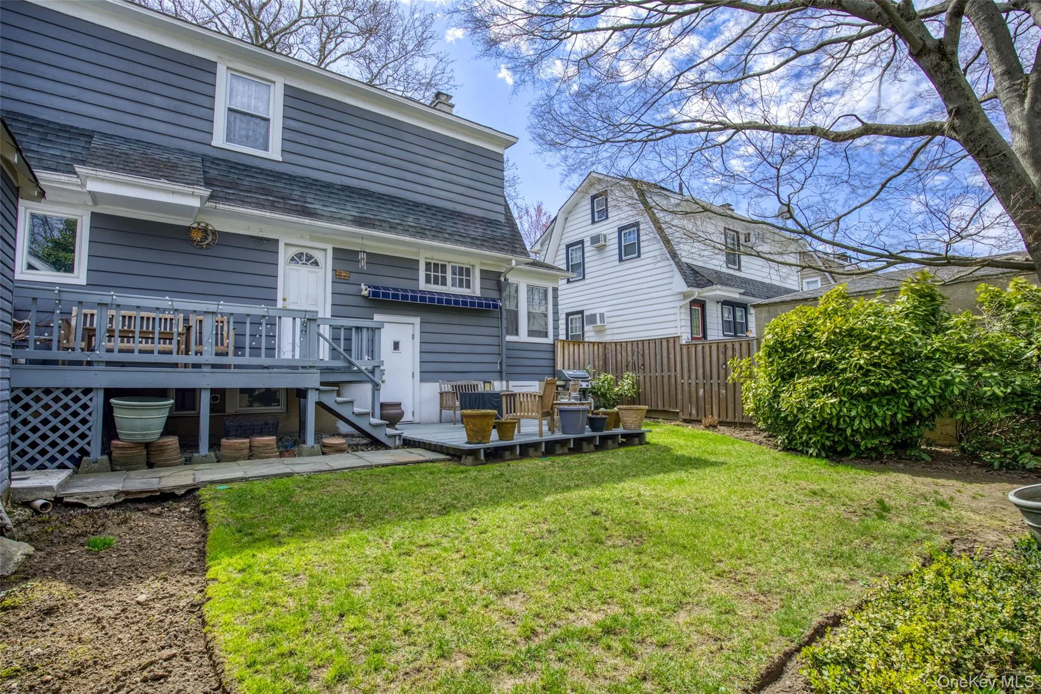 Rear exterior featuring blue siding, an elevated wood deck, a ground-level wood patio, a green lawn, and mature trees Rear exterior featuring blue siding, an elevated wood deck, a ground-level wood patio, a green lawn, and mature trees