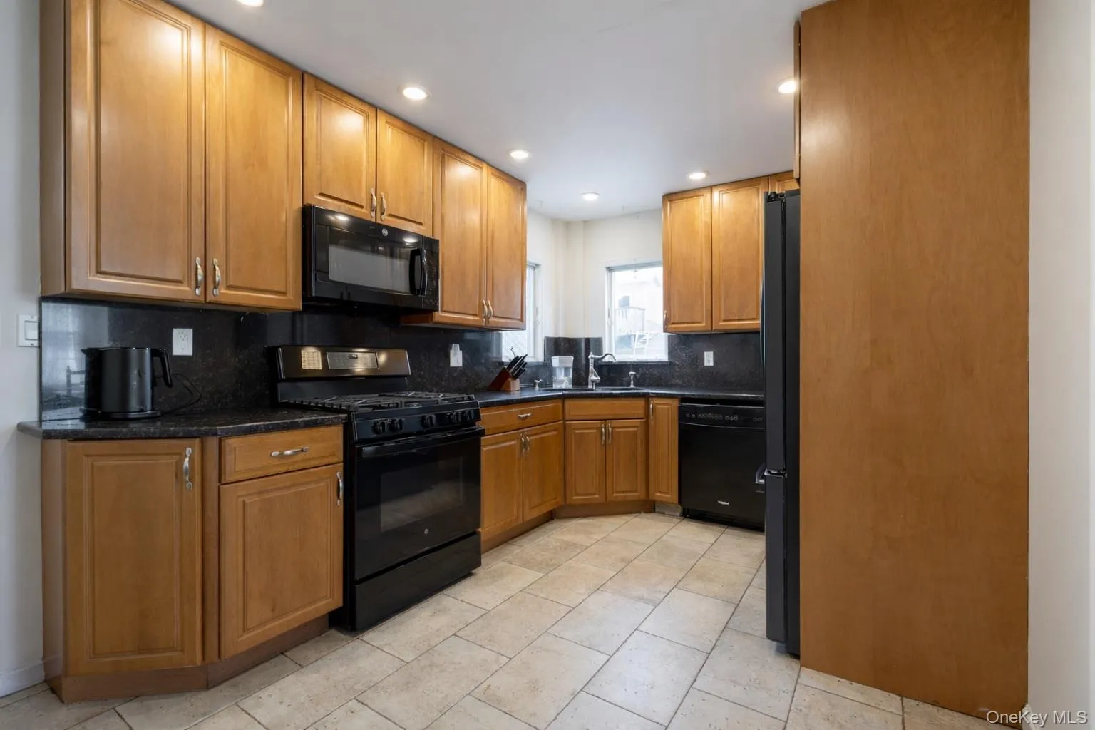Kitchen featuring wood cabinetry, black appliances, dark countertops, and tile flooring Kitchen featuring wood cabinetry, black appliances, dark countertops, and tile flooring