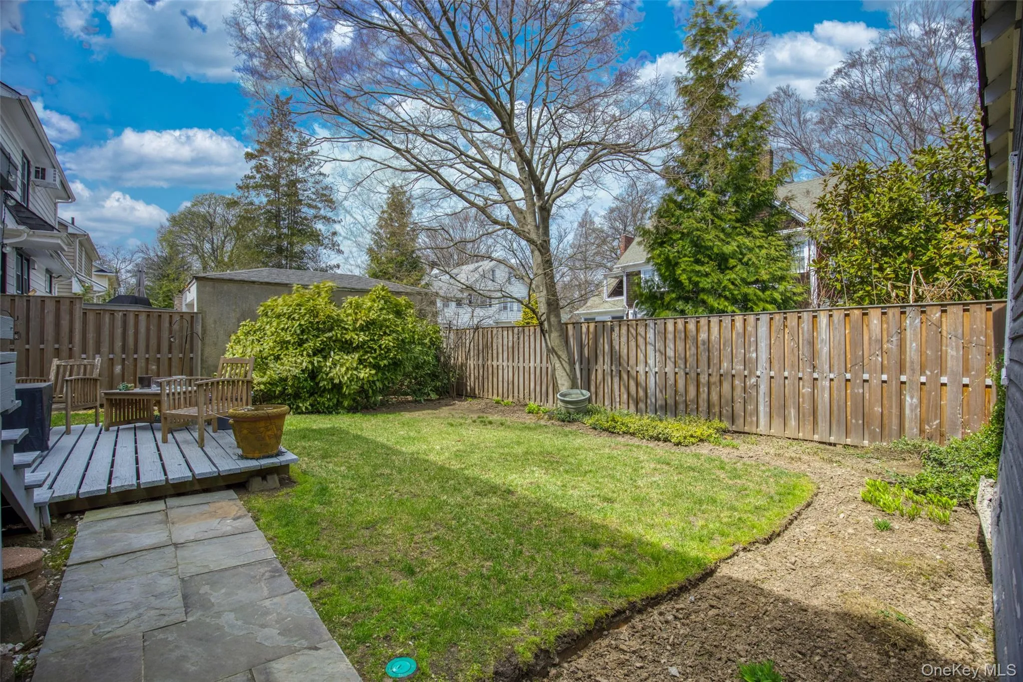 Rear yard featuring a wooden deck, stone patio, and grassy area with surrounding planting beds Rear yard featuring a wooden deck, stone patio, and grassy area with surrounding planting beds