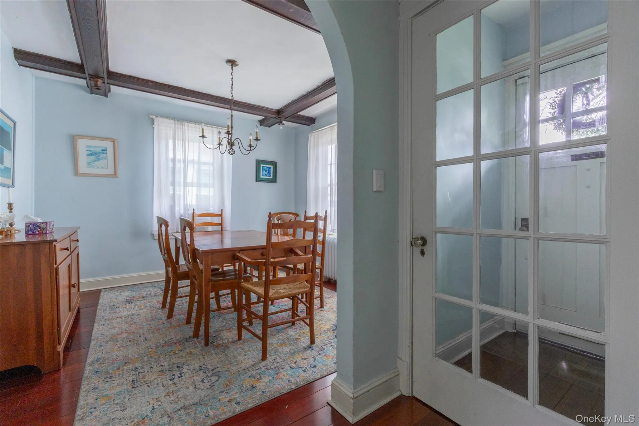 Dining area featuring exposed ceiling beams, a chandelier light fixture, wood-finish flooring, and an arched entryway Dining area featuring exposed ceiling beams, a chandelier light fixture, wood-finish flooring, and an arched entryway