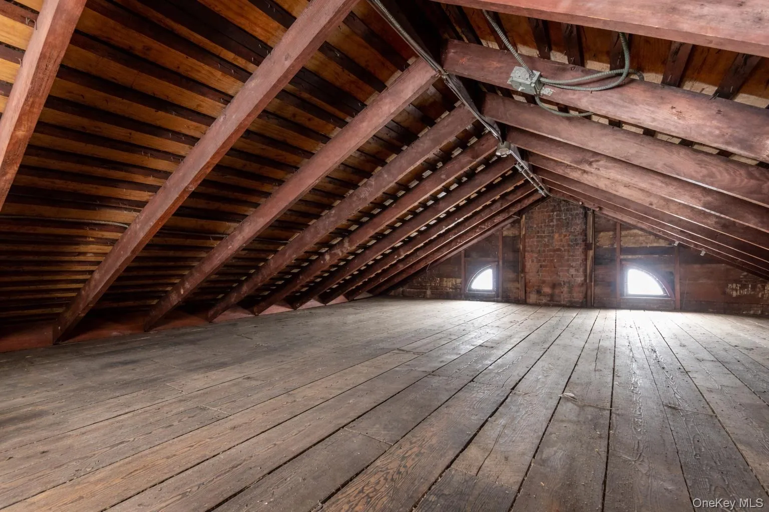 Spacious attic area featuring exposed wood beams and plank flooring Spacious attic area featuring exposed wood beams and plank flooring