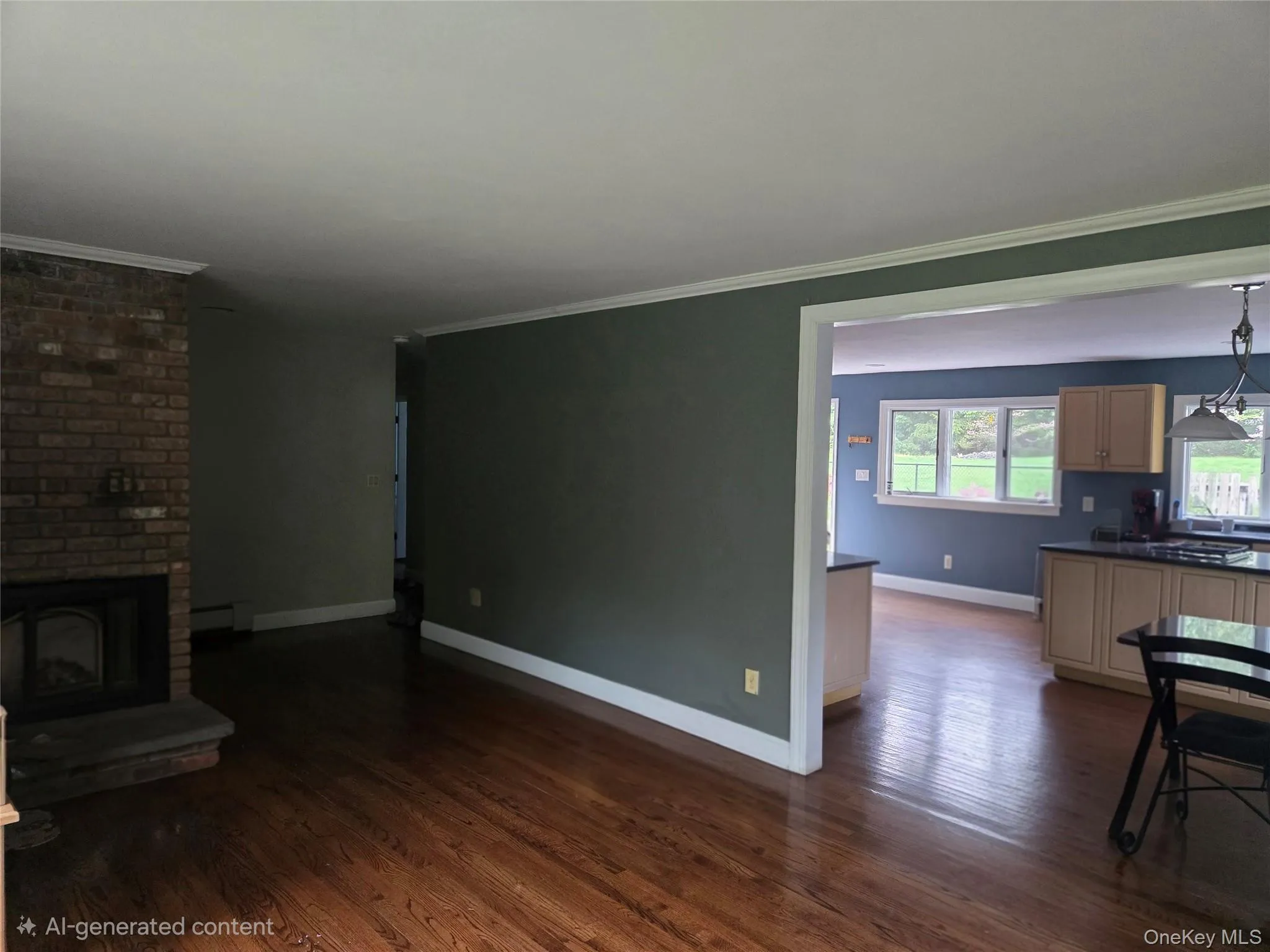 Hardwood flooring throughout, featuring a brick fireplace with stone hearth and an open concept layout into a kitchen with light wood cabinetry and dark countertops Hardwood flooring throughout, featuring a brick fireplace with stone hearth and an open concept layout into a kitchen with light wood cabinetry and dark countertops