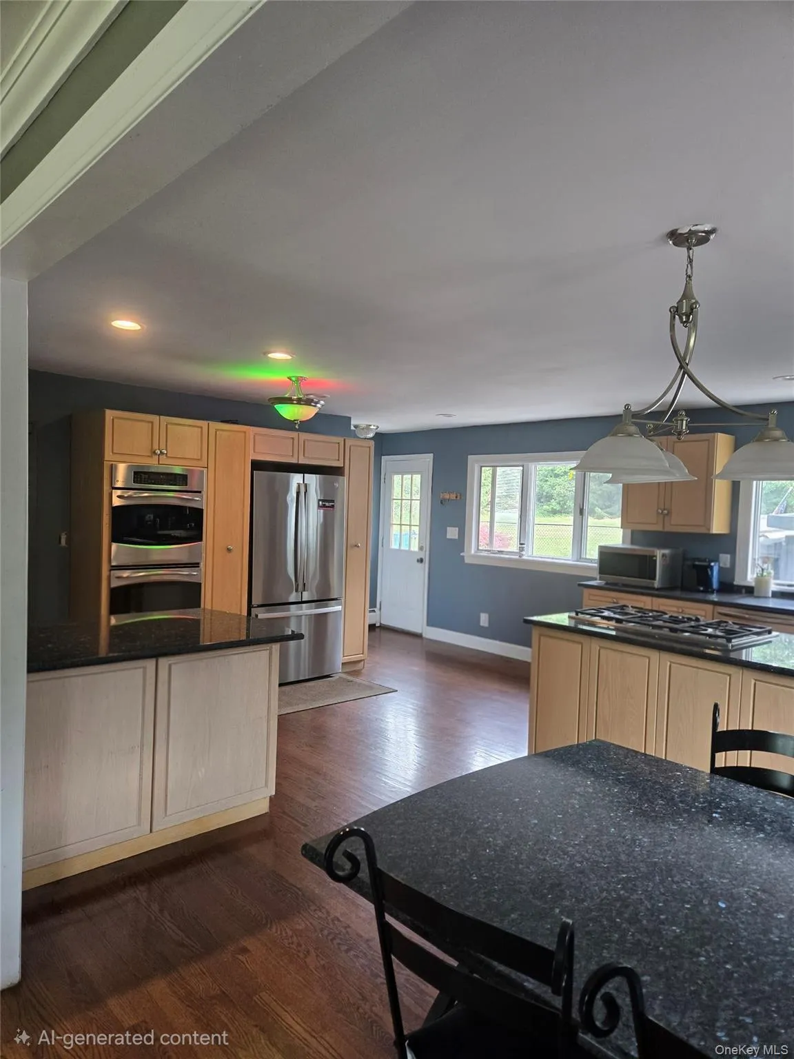 Kitchen featuring wood-finish flooring, two kitchen islands with dark countertops, built-in double ovens, and stainless steel appliances Kitchen featuring wood-finish flooring, two kitchen islands with dark countertops, built-in double ovens, and stainless steel appliances