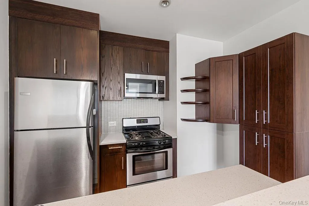 Kitchen featuring dark wood-finish cabinetry, stainless steel appliances, and a mosaic tile backsplash Kitchen featuring dark wood-finish cabinetry, stainless steel appliances, and a mosaic tile backsplash