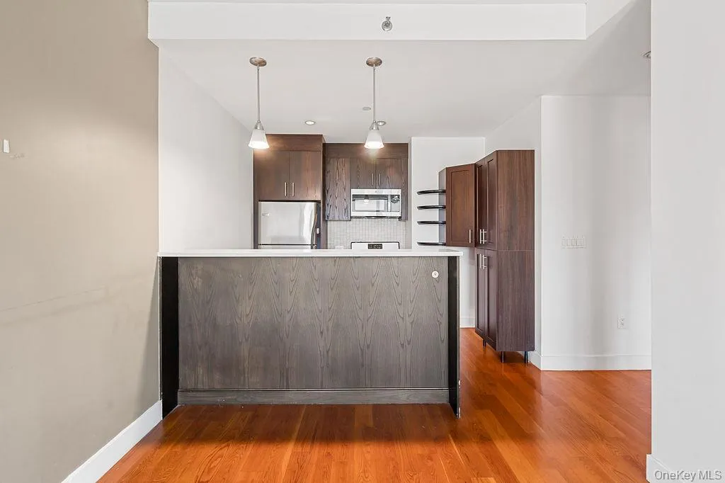 Kitchen island with a light-toned countertop, wood-finish flooring, dark wood cabinetry, stainless steel appliances, and pendant lighting Kitchen island with a light-toned countertop, wood-finish flooring, dark wood cabinetry, stainless steel appliances, and pendant lighting