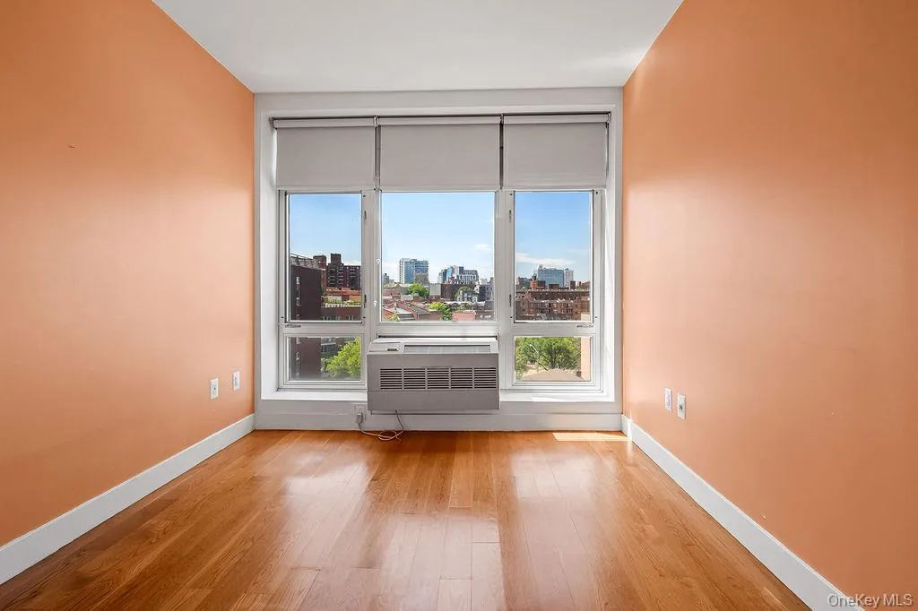 Room featuring a large window with urban scenery, wood-finish flooring, and light-toned walls Room featuring a large window with urban scenery, wood-finish flooring, and light-toned walls