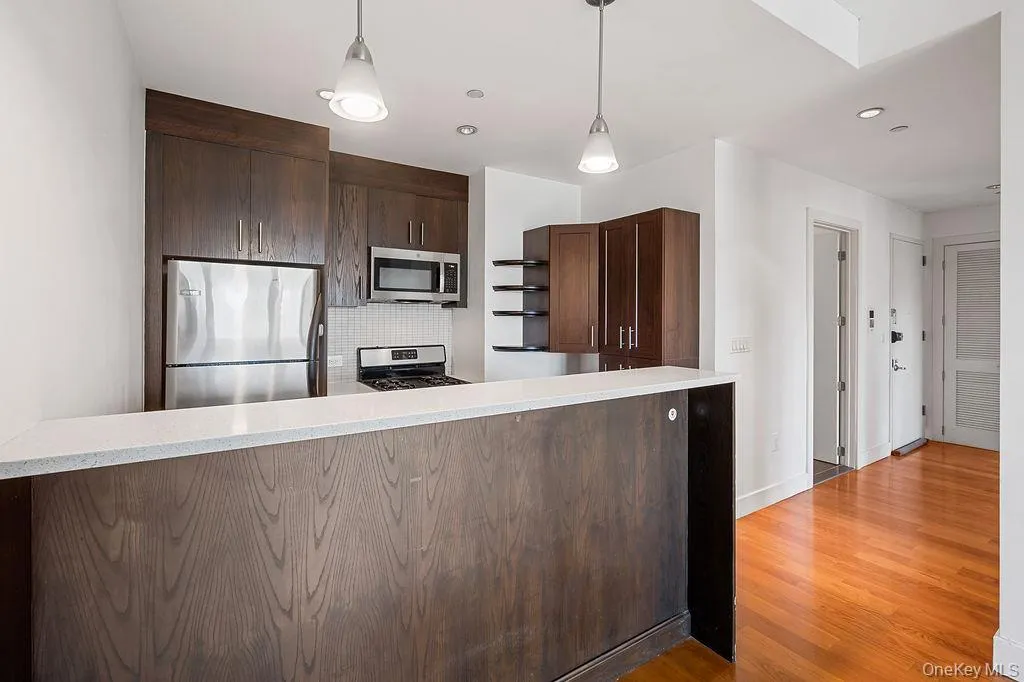 Kitchen featuring dark wood-finish cabinetry, stainless steel appliances, white tile backsplash, and light-colored countertop Kitchen featuring dark wood-finish cabinetry, stainless steel appliances, white tile backsplash, and light-colored countertop