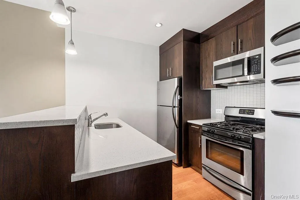 Modern kitchen featuring dark wood-finish cabinetry, stainless steel appliances, white quartz countertops, and a subway tile backsplash Modern kitchen featuring dark wood-finish cabinetry, stainless steel appliances, white quartz countertops, and a subway tile backsplash