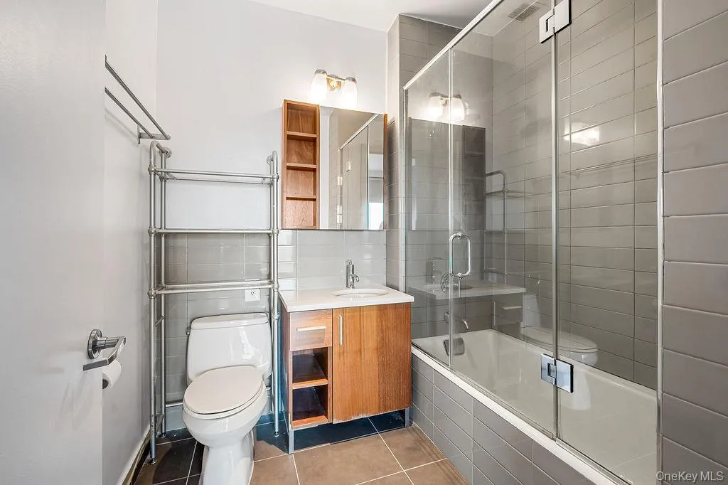 Modern bathroom featuring a soaking tub with glass enclosure, subway tile shower surround, and a wood-finish vanity with an integrated sink Modern bathroom featuring a soaking tub with glass enclosure, subway tile shower surround, and a wood-finish vanity with an integrated sink