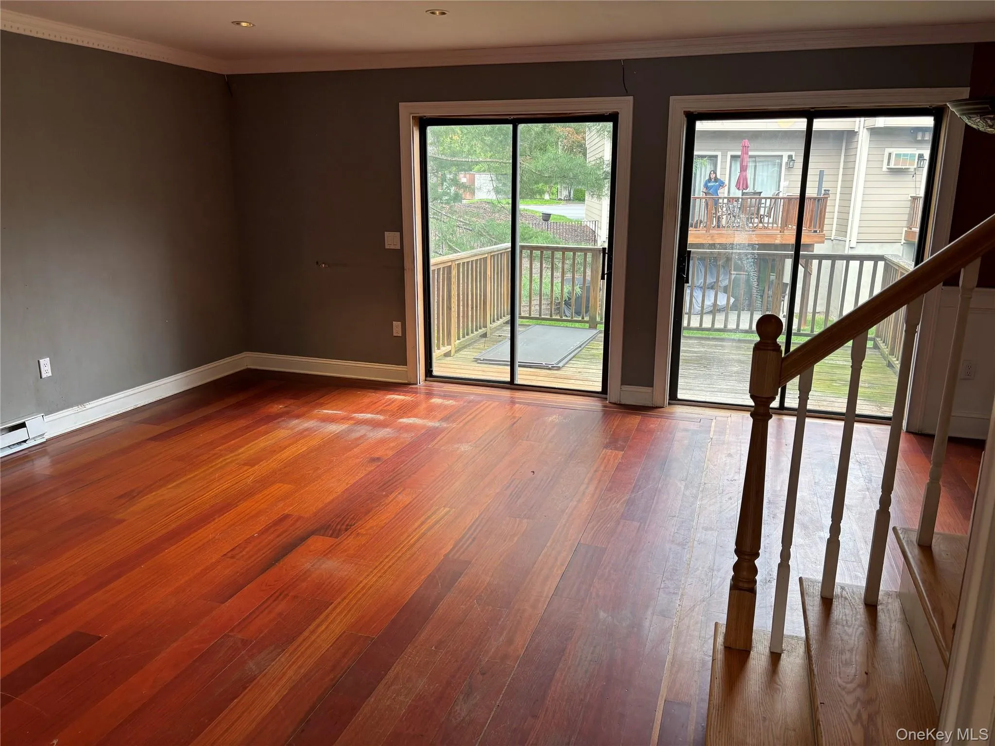 Spacious room featuring wood-finish flooring, two sliding glass doors, and a wood railing staircase Spacious room featuring wood-finish flooring, two sliding glass doors, and a wood railing staircase