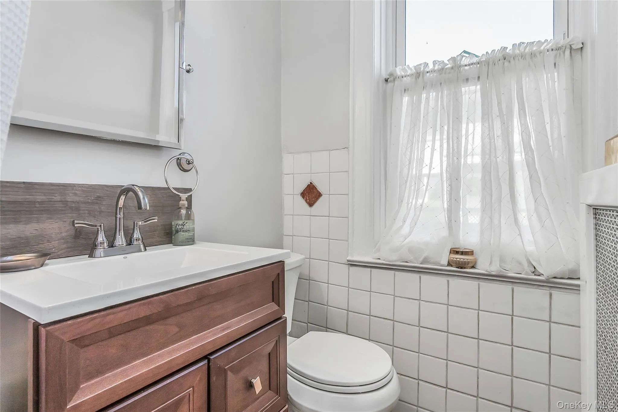 Bathroom decorated with white fixtures, decorative tile and wood vanity Bathroom decorated with white fixtures, decorative tile and wood vanity