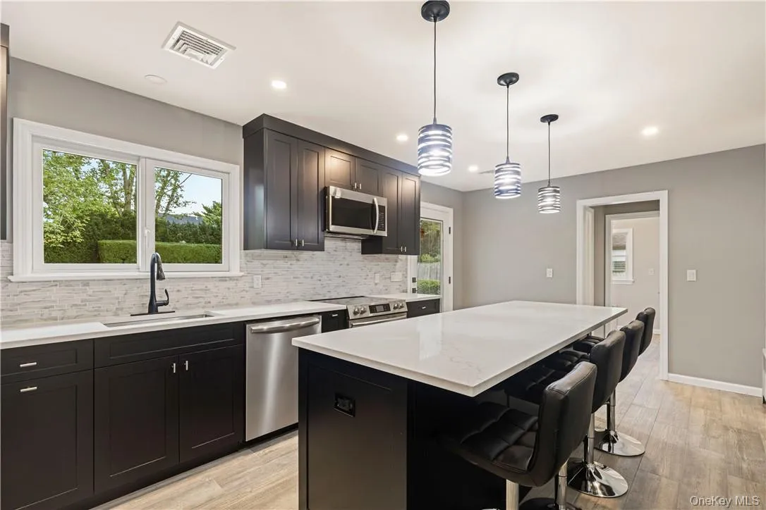 Kitchen with stainless steel finishes, hanging light fixtures, a center island, decorative backsplash, door to yard Kitchen with stainless steel finishes, hanging light fixtures, a center island, decorative backsplash, door to yard