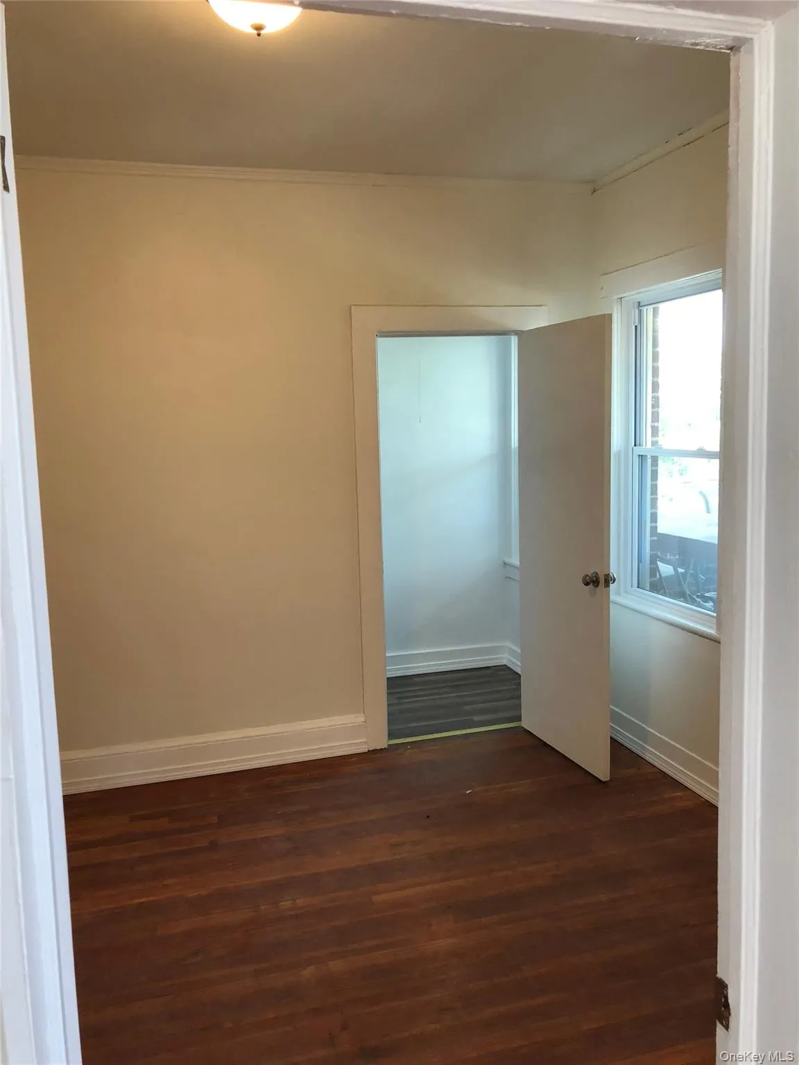 Bedroom featuring rich wood-finish flooring, light-toned wall paint, white trim, and a ceiling-mounted light fixture Bedroom featuring rich wood-finish flooring, light-toned wall paint, white trim, and a ceiling-mounted light fixture