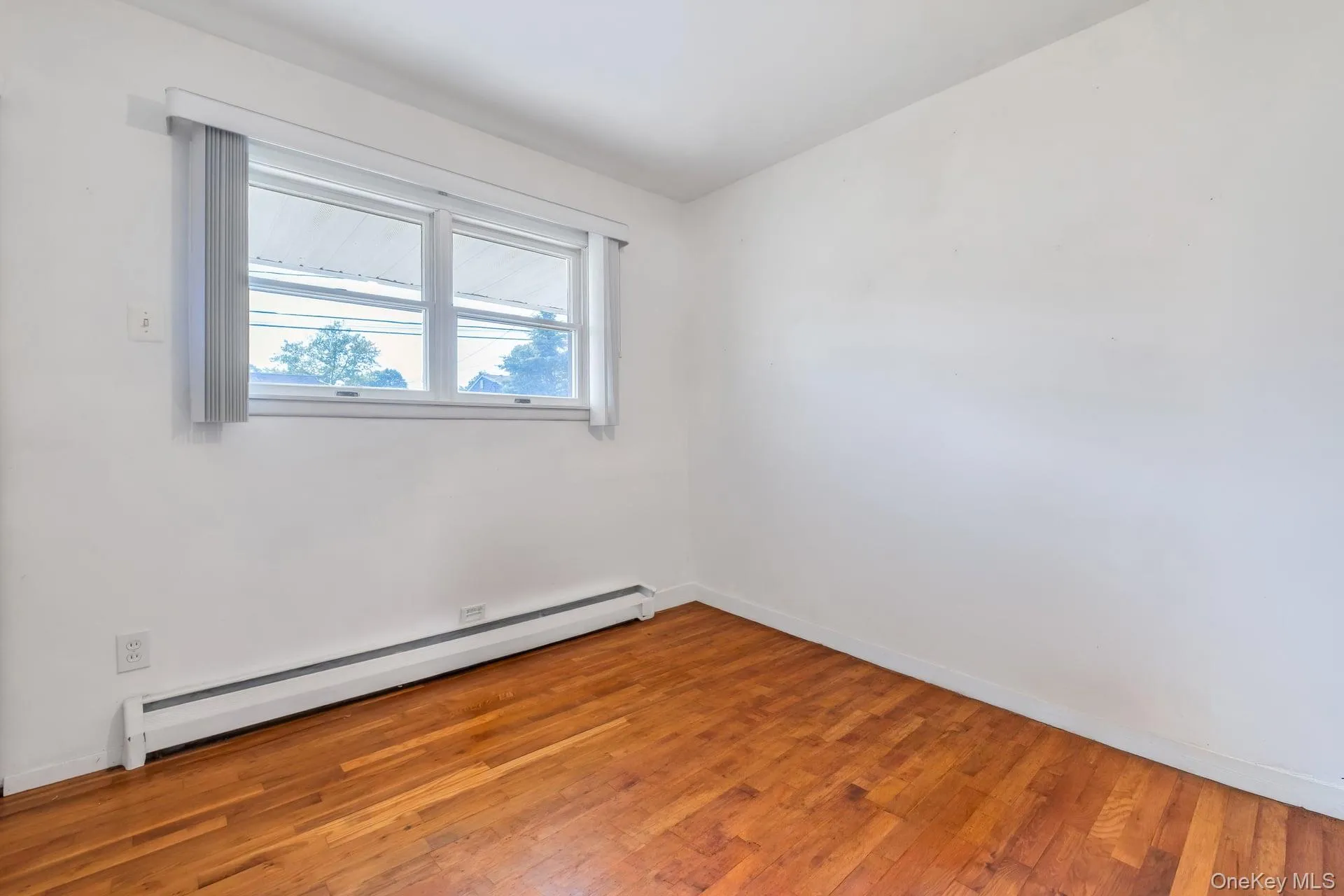 Interior room featuring wood-finish flooring, white painted walls, and a window with blinds Interior room featuring wood-finish flooring, white painted walls, and a window with blinds