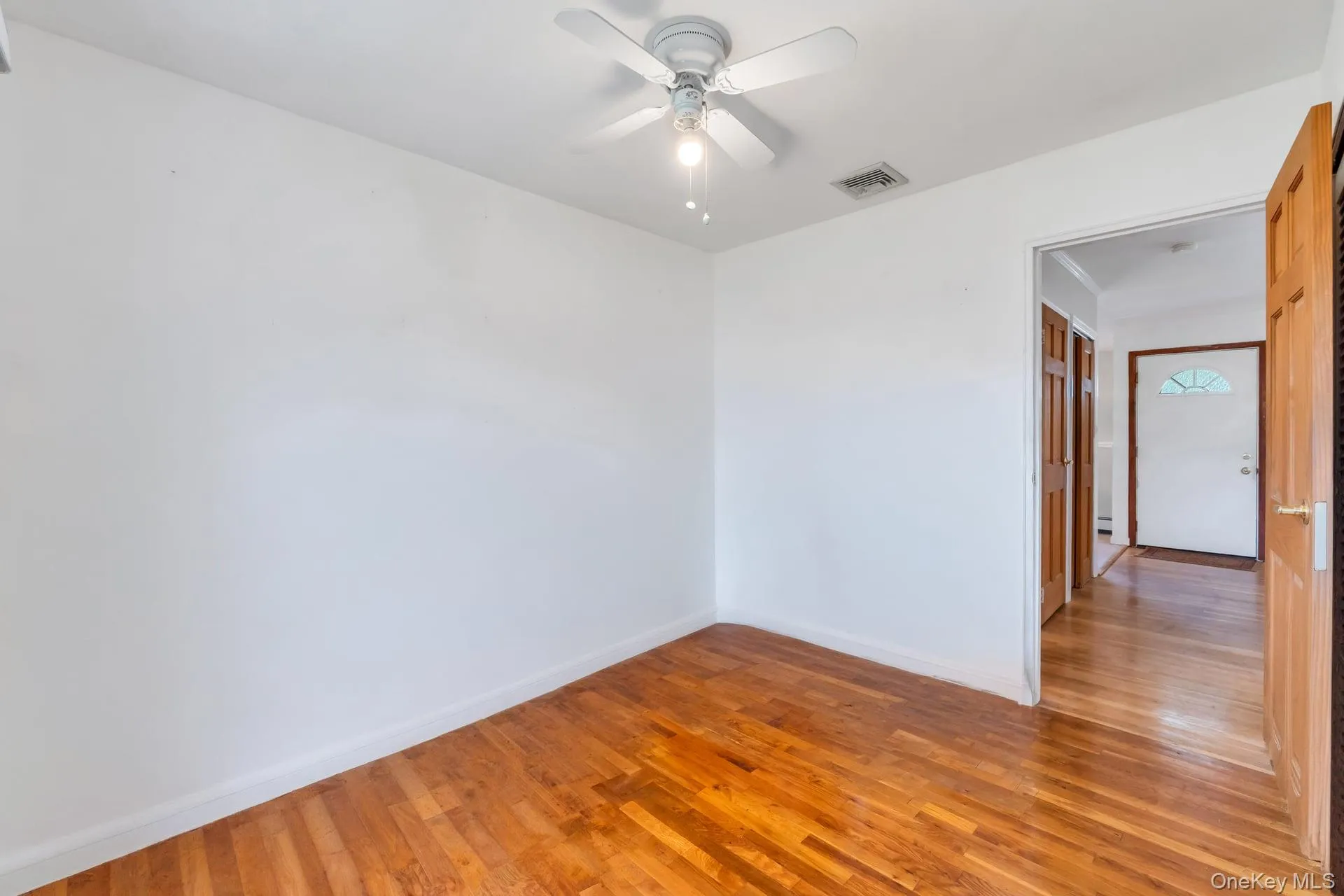 Interior room featuring wood-finish flooring, white painted walls, and a ceiling fan with integrated lighting Interior room featuring wood-finish flooring, white painted walls, and a ceiling fan with integrated lighting