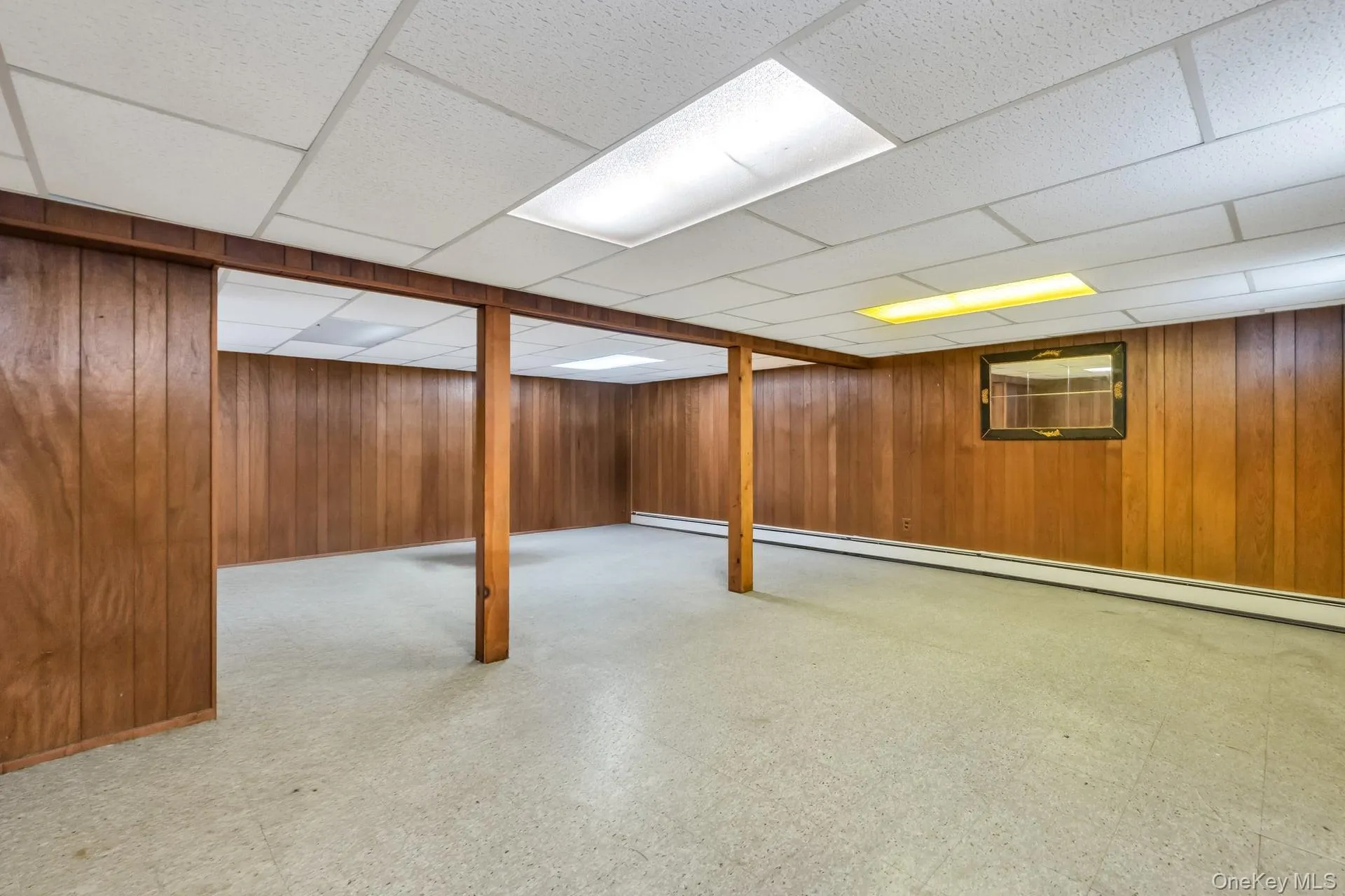 Spacious room featuring wood-finish paneling, a drop ceiling with integrated lighting, and light-colored flooring Spacious room featuring wood-finish paneling, a drop ceiling with integrated lighting, and light-colored flooring