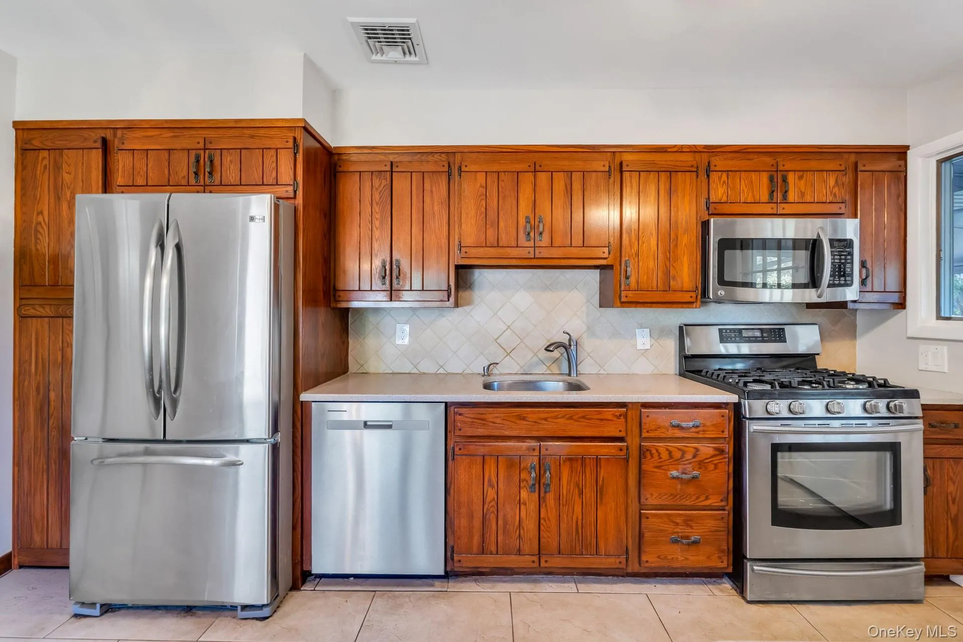 Kitchen featuring wood cabinetry, stainless steel appliances, a tiled backsplash, and light-toned countertops Kitchen featuring wood cabinetry, stainless steel appliances, a tiled backsplash, and light-toned countertops
