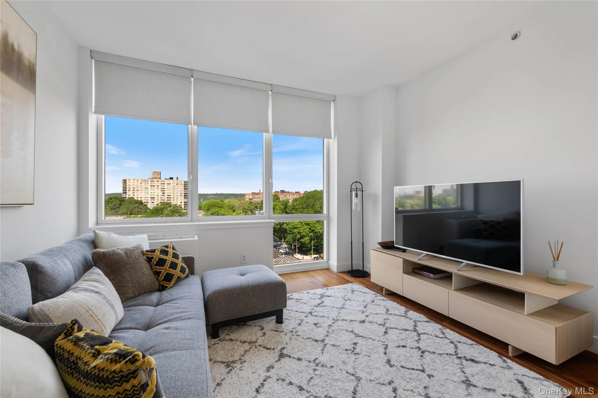 Expansive window wall with roller shades, hardwood flooring, recessed ceiling lighting, light wood-finish media console, and white walls Expansive window wall with roller shades, hardwood flooring, recessed ceiling lighting, light wood-finish media console, and white walls