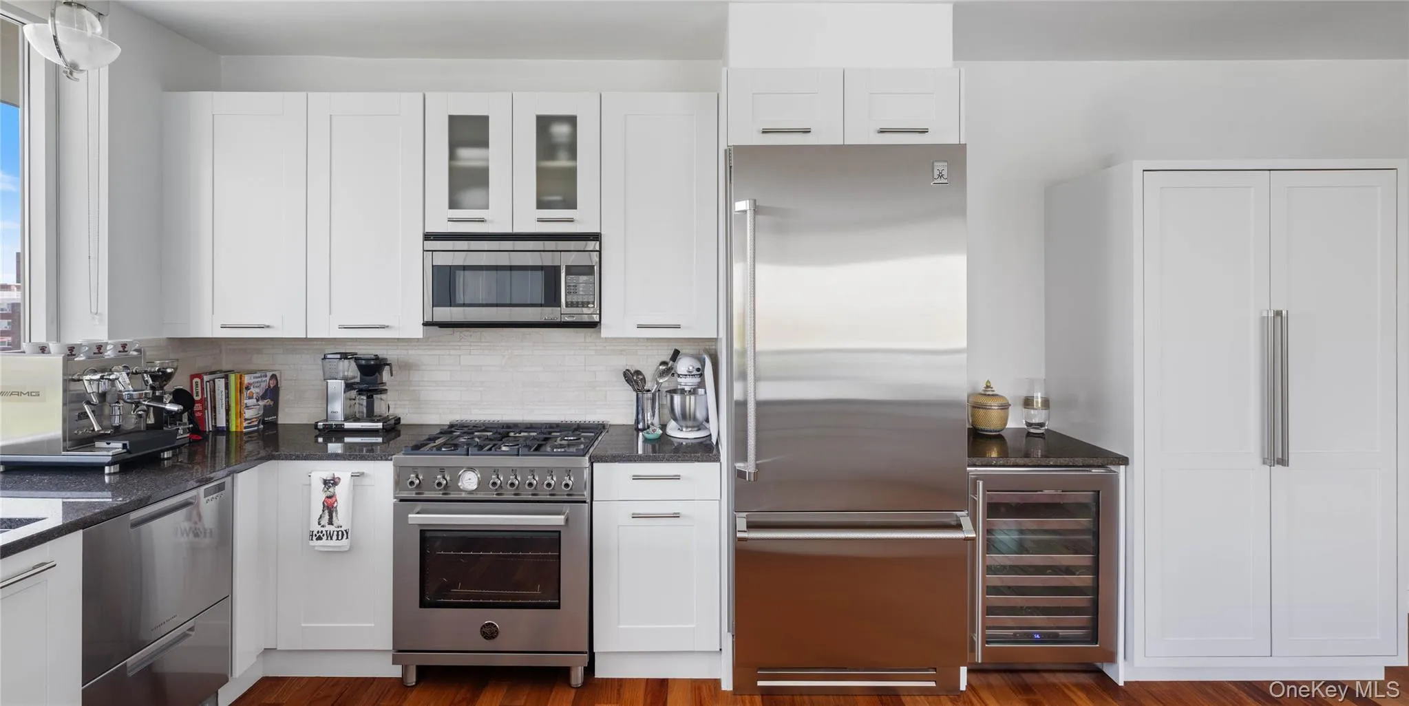 Contemporary kitchen featuring white cabinetry, dark stone countertops, stainless steel appliances, and wood-finish flooring Contemporary kitchen featuring white cabinetry, dark stone countertops, stainless steel appliances, and wood-finish flooring
