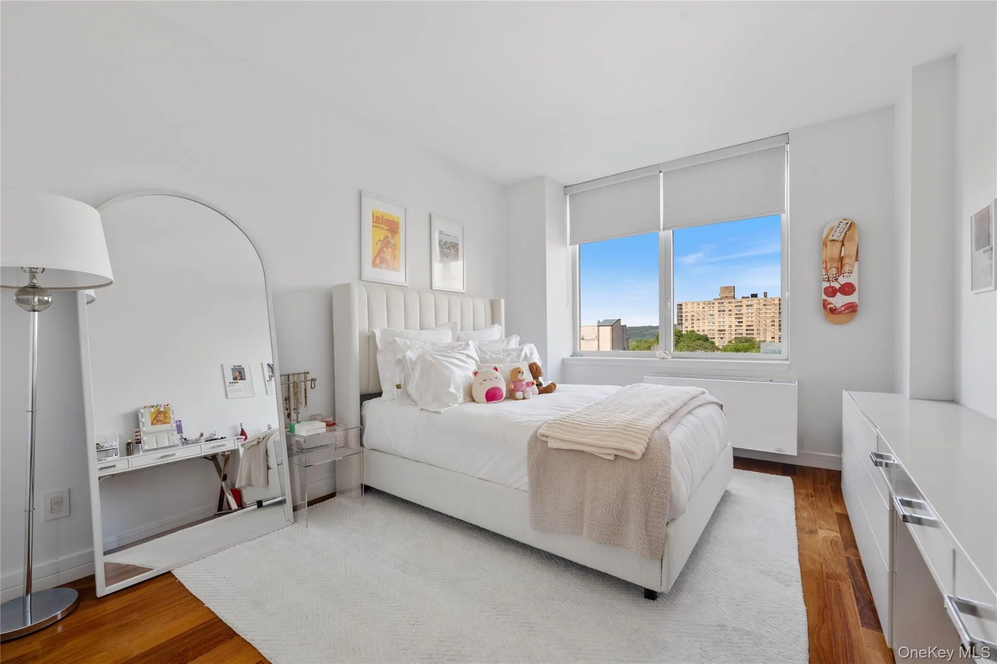 Room featuring wood-finish flooring, white walls, and a large window with roller shades Room featuring wood-finish flooring, white walls, and a large window with roller shades