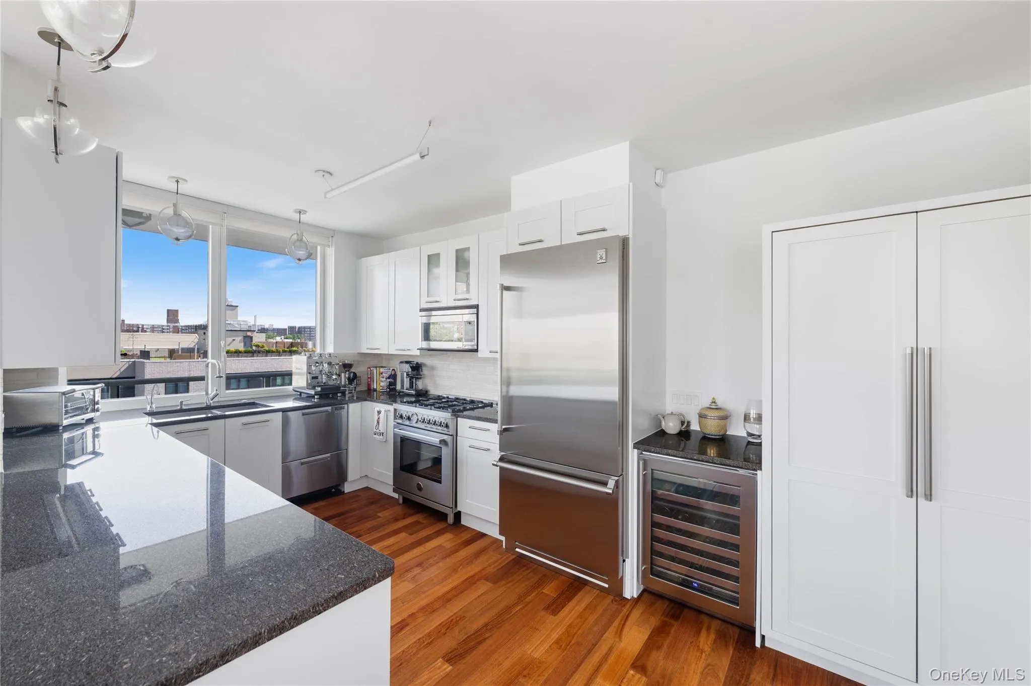 Gourmet kitchen featuring a large island with a dark stone countertop, stainless steel appliances, white cabinetry, and wood-finish flooring Gourmet kitchen featuring a large island with a dark stone countertop, stainless steel appliances, white cabinetry, and wood-finish flooring