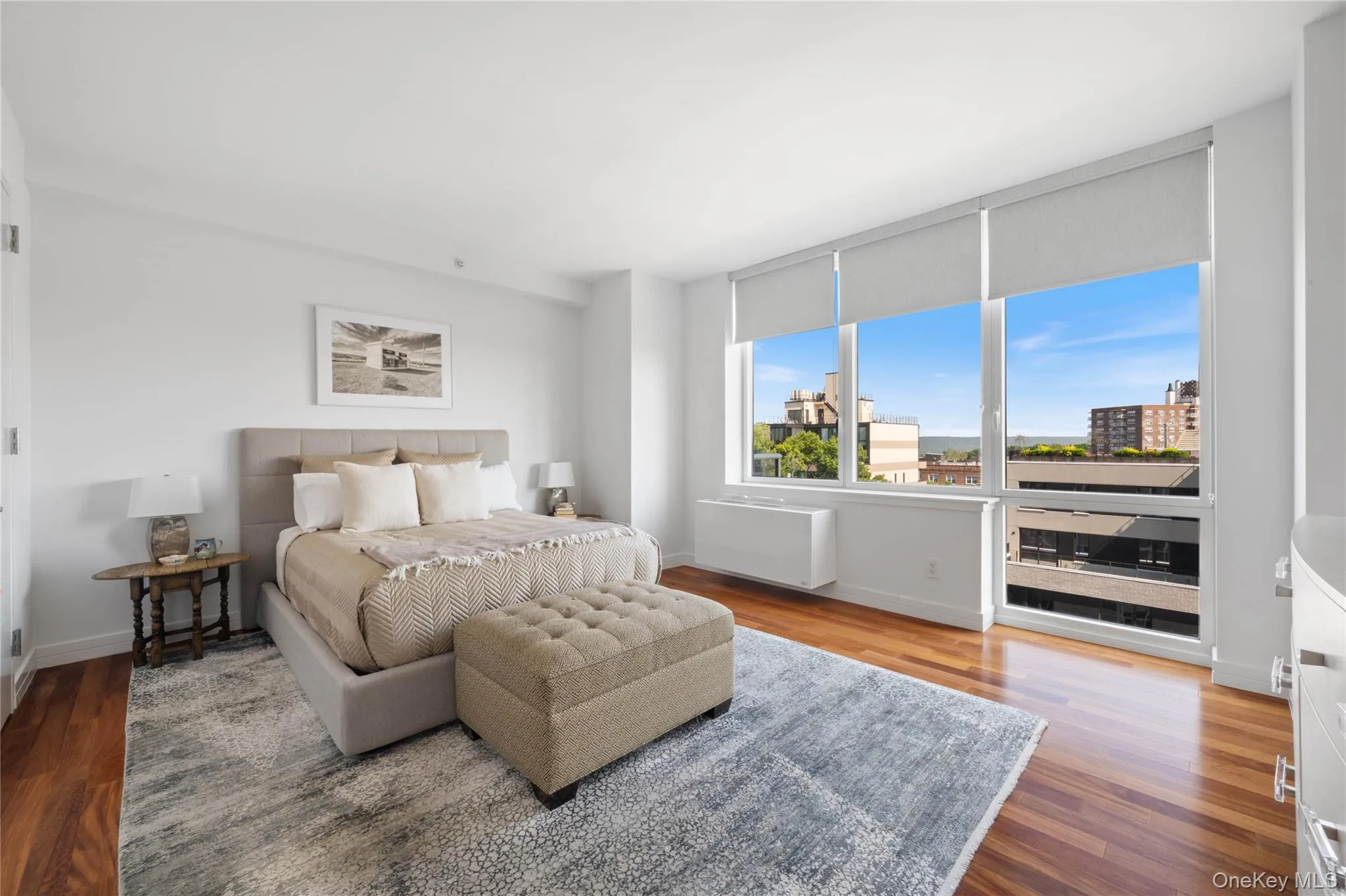 Bright room with extensive window system featuring roller shades, wood-finish flooring, and white walls Bright room with extensive window system featuring roller shades, wood-finish flooring, and white walls