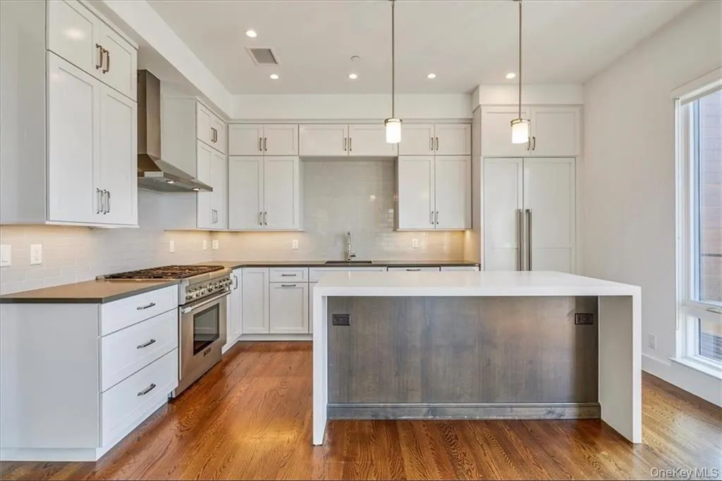 Contemporary kitchen featuring an expansive center island with a wood-finish base, ample white cabinetry, stainless steel appliances, and wood-finish flooring Contemporary kitchen featuring an expansive center island with a wood-finish base, ample white cabinetry, stainless steel appliances, and wood-finish flooring
