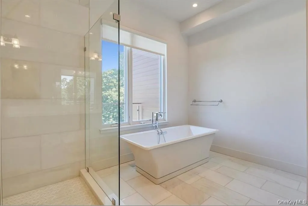 Freestanding soaking tub with chrome fixtures positioned beneath a window, complemented by a glass-enclosed shower with tiled walls and mosaic flooring Freestanding soaking tub with chrome fixtures positioned beneath a window, complemented by a glass-enclosed shower with tiled walls and mosaic flooring