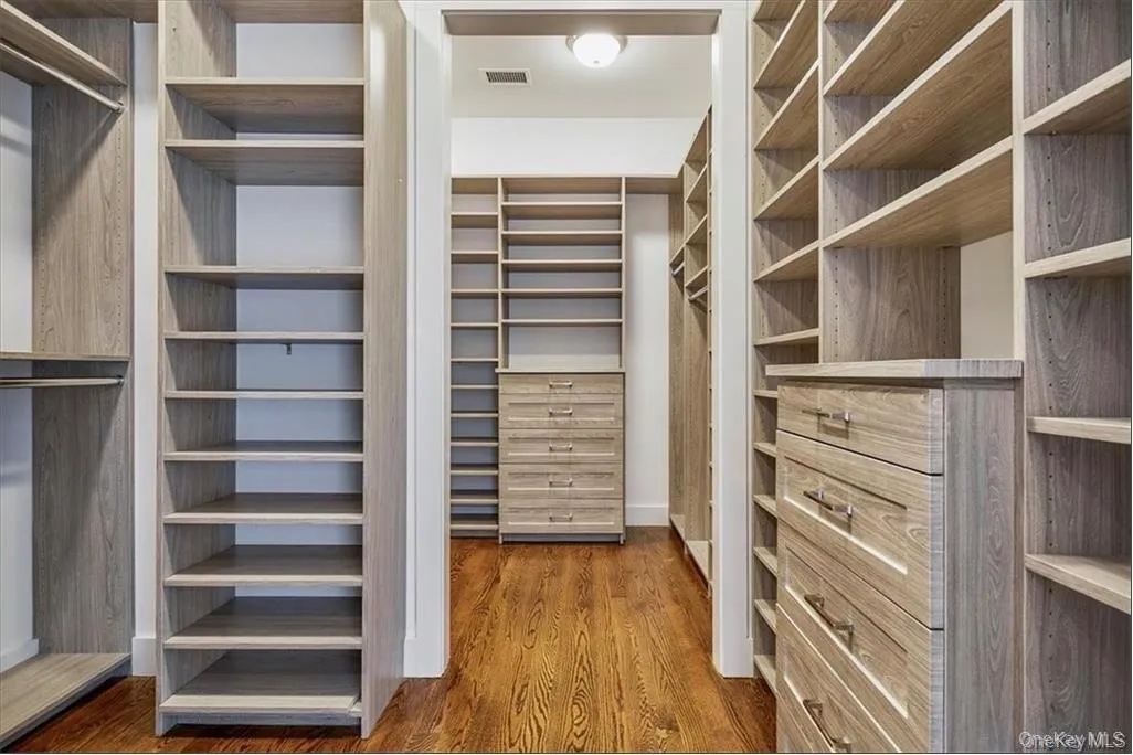 Spacious walk-in closet featuring extensive built-in shelving, integrated drawer units with brushed nickel hardware, multiple hanging rods, and rich wood-finish flooring Spacious walk-in closet featuring extensive built-in shelving, integrated drawer units with brushed nickel hardware, multiple hanging rods, and rich wood-finish flooring