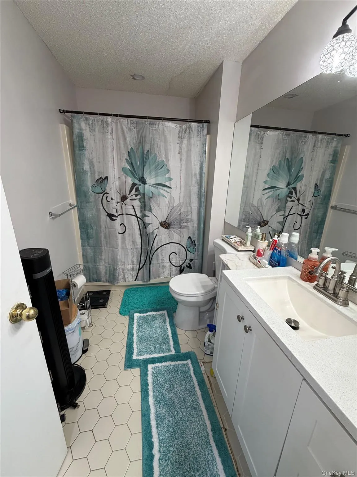 Bathroom featuring hexagonal tile flooring, a white vanity with an integrated sink, a large wall-mounted mirror, and a toilet Bathroom featuring hexagonal tile flooring, a white vanity with an integrated sink, a large wall-mounted mirror, and a toilet