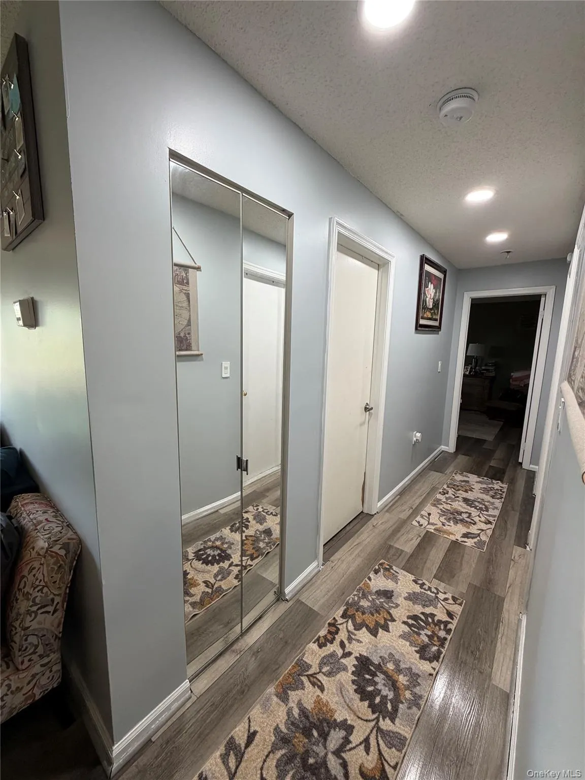 Hallway featuring wood-finish flooring, recessed lighting, and a mirrored closet door Hallway featuring wood-finish flooring, recessed lighting, and a mirrored closet door