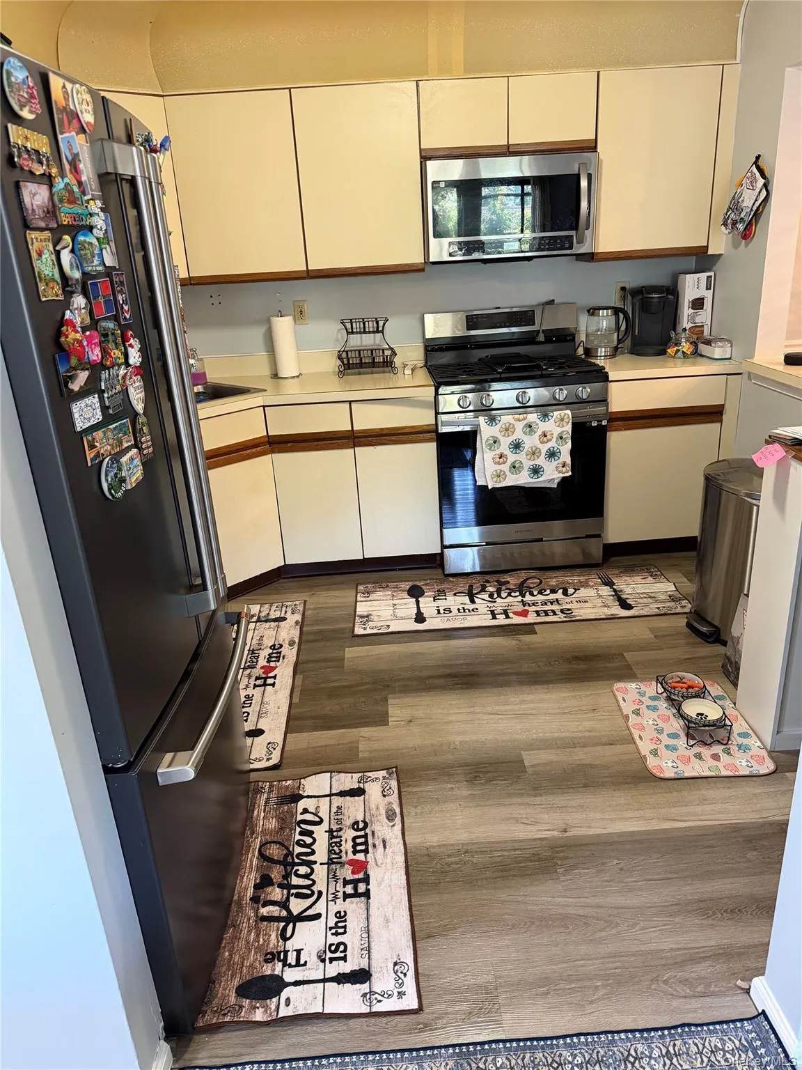 Kitchen featuring wood-finish flooring, white cabinetry, and stainless steel appliances including a refrigerator, microwave, and range Kitchen featuring wood-finish flooring, white cabinetry, and stainless steel appliances including a refrigerator, microwave, and range