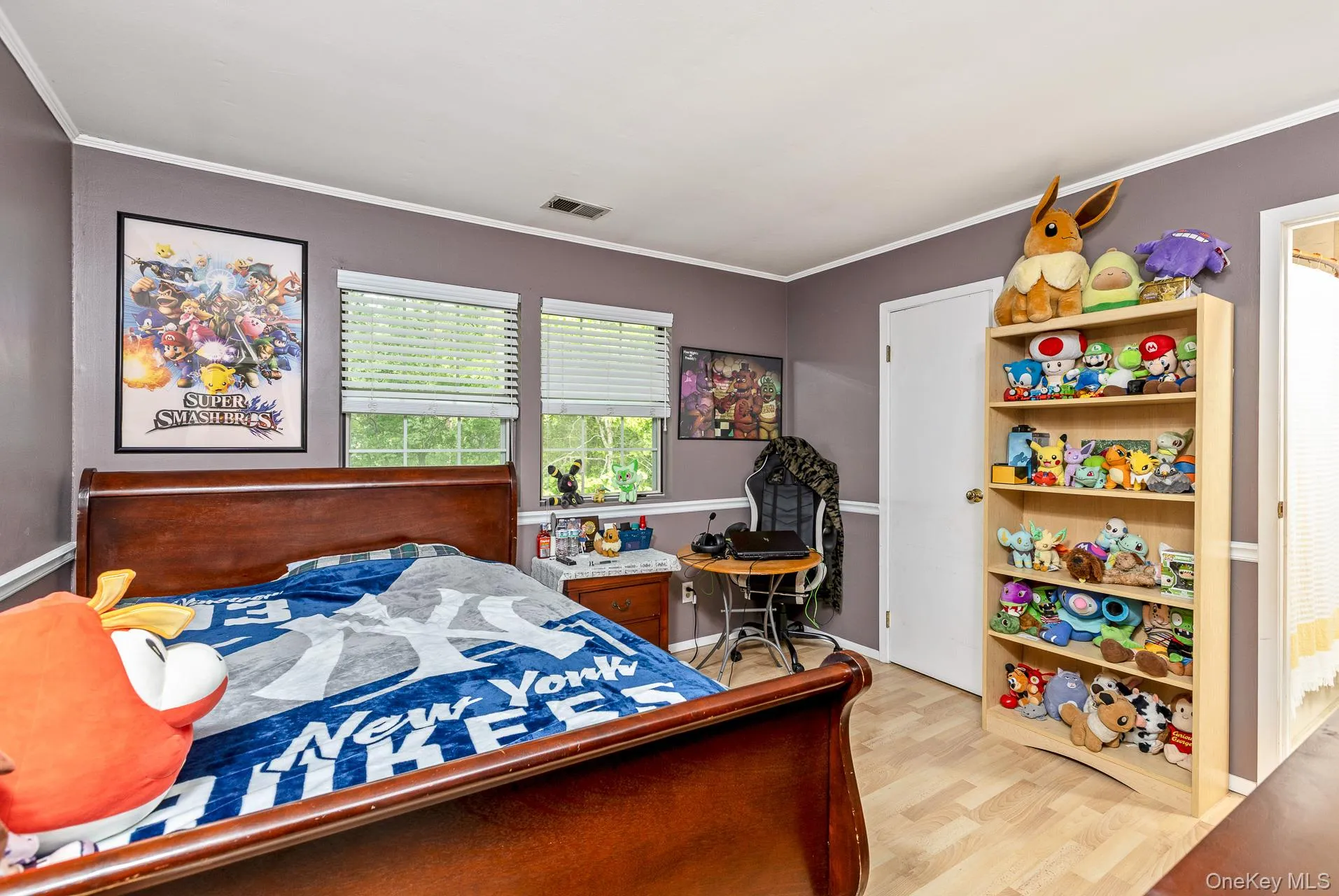 Bedroom featuring wood-finish flooring, two windows with blinds, a white door, and a built-in shelving unit Bedroom featuring wood-finish flooring, two windows with blinds, a white door, and a built-in shelving unit