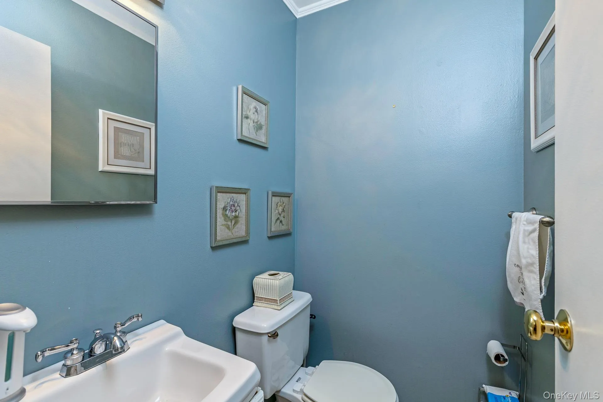 Powder room with a pedestal sink, chrome faucet, wall-mounted mirror, and a white toilet Powder room with a pedestal sink, chrome faucet, wall-mounted mirror, and a white toilet