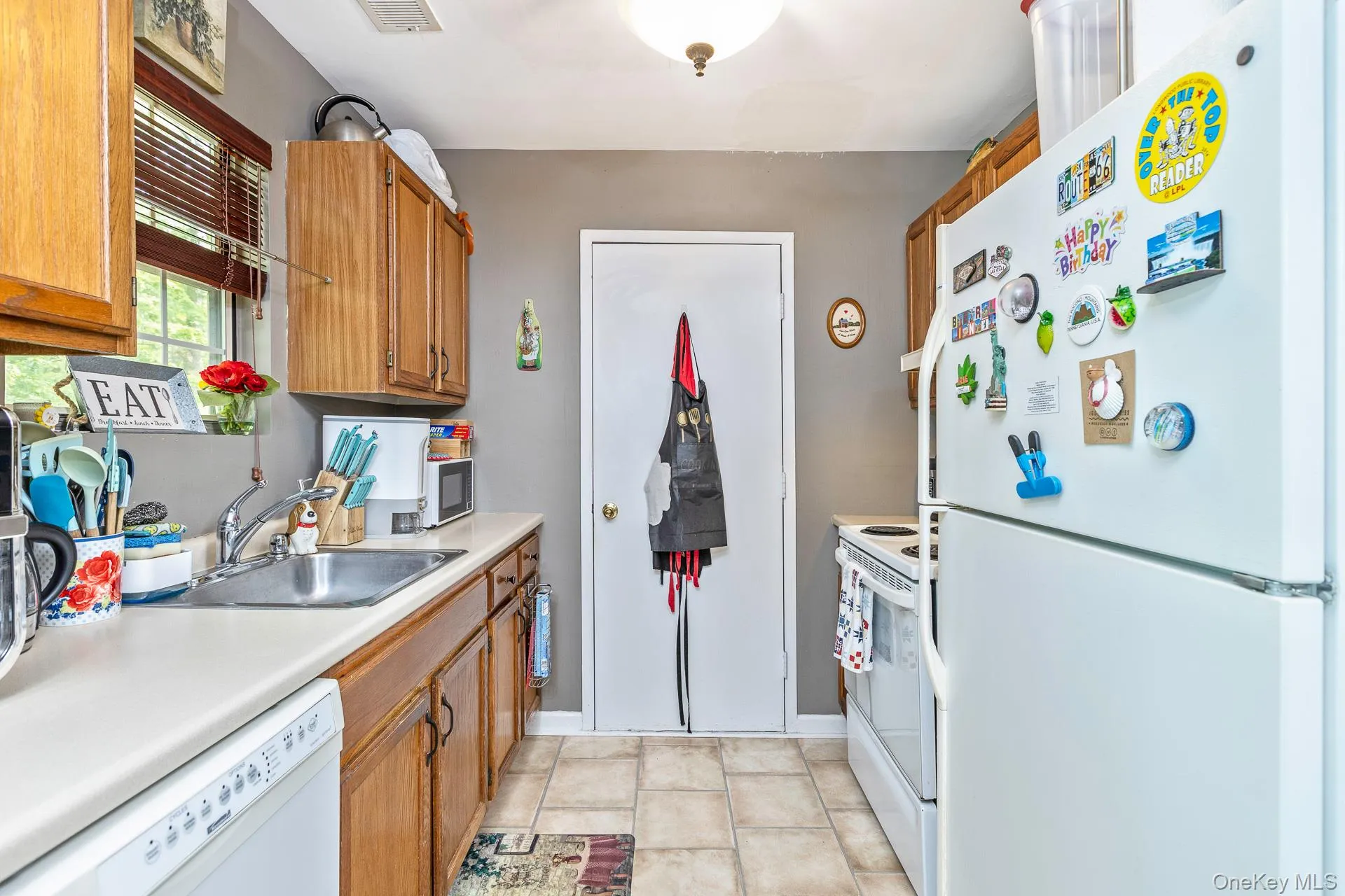Kitchen featuring a double-basin stainless steel sink, wood cabinetry, white countertops, and a white dishwasher Kitchen featuring a double-basin stainless steel sink, wood cabinetry, white countertops, and a white dishwasher