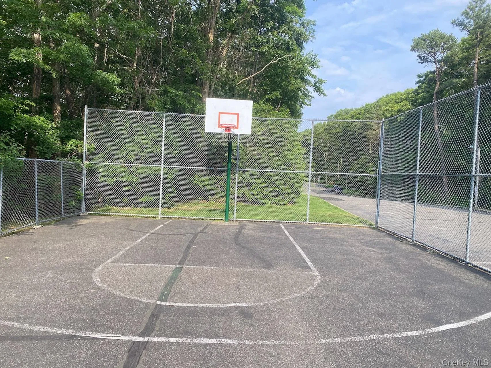 Paved sports court featuring a chain-link fence enclosure and a freestanding basketball hoop Paved sports court featuring a chain-link fence enclosure and a freestanding basketball hoop