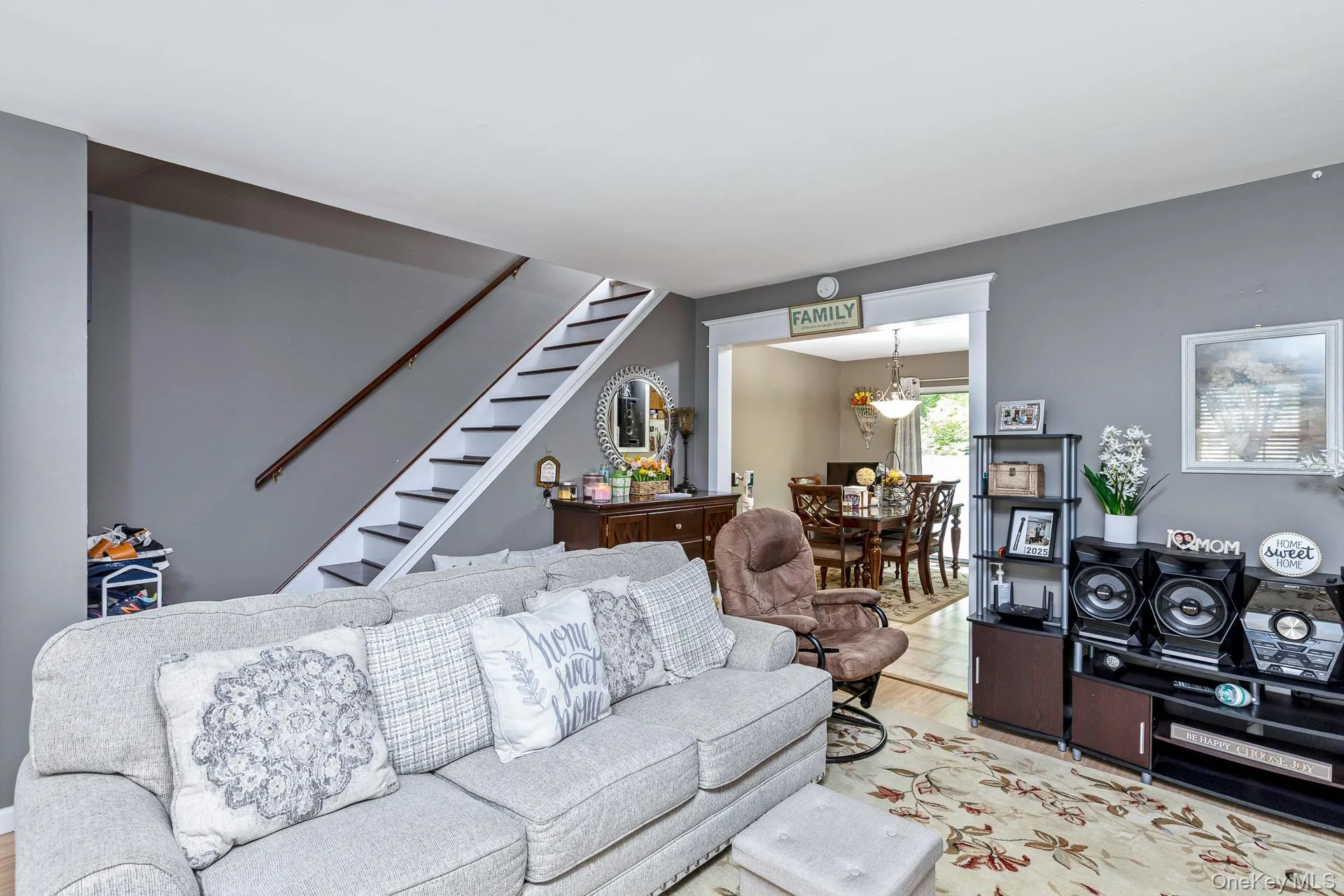 Living area featuring a staircase with dark treads and a wood handrail, light gray walls, and a broad archway opening to a dining space Living area featuring a staircase with dark treads and a wood handrail, light gray walls, and a broad archway opening to a dining space